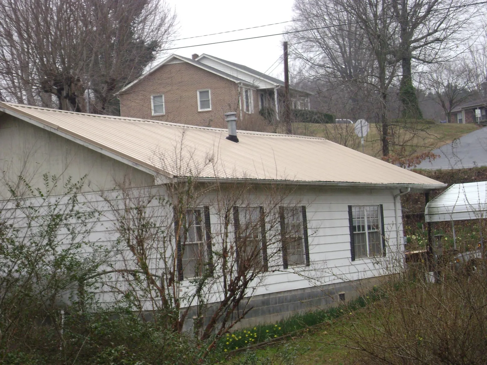 Tan metal roof on a white sided house set into a hillside — Commercial Roofing by Roofing Brothers in Woodbine